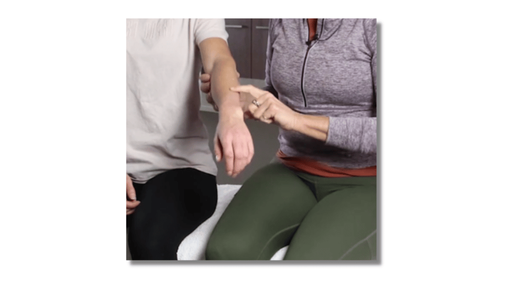 A remedial massage therapist gliding down a finger over the wrist of the patient